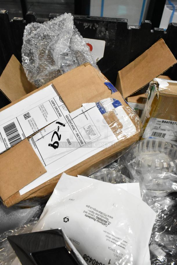 Lot of various items in a black poly bin, including packages, bubble wrap, and a GMC emblem. Mixed condition.