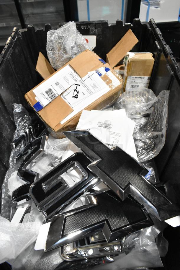 Lot of assorted items in black poly bin, featuring a prominent GMC emblem. Various packaging and labels included.