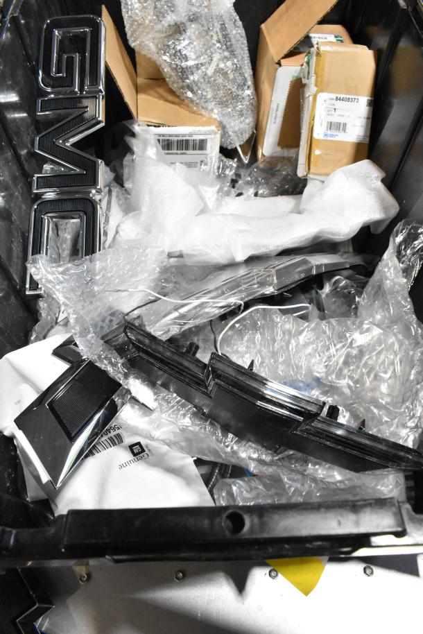 Lot with GMC emblem, various car parts in black poly bin. Includes packaging materials, possible spare parts. Condition varies.