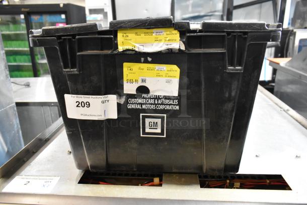 Black poly bin containing various items, labeled "Property of Customer Care & Aftersales, General Motors Corporation," lot number 209.