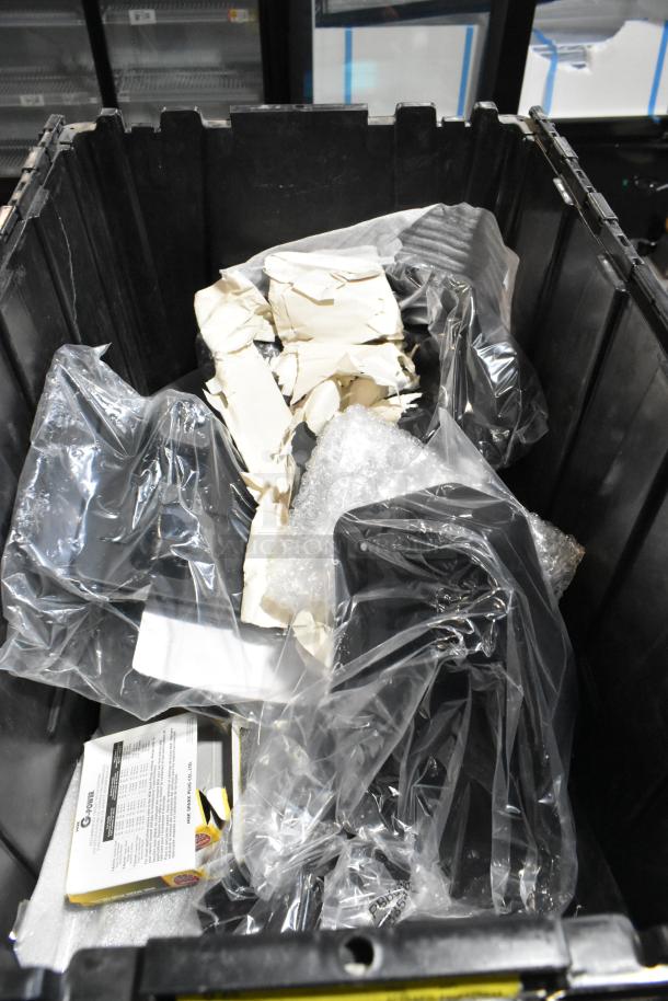 Black poly bin containing assorted items, including packaging materials and boxed product, varying condition.