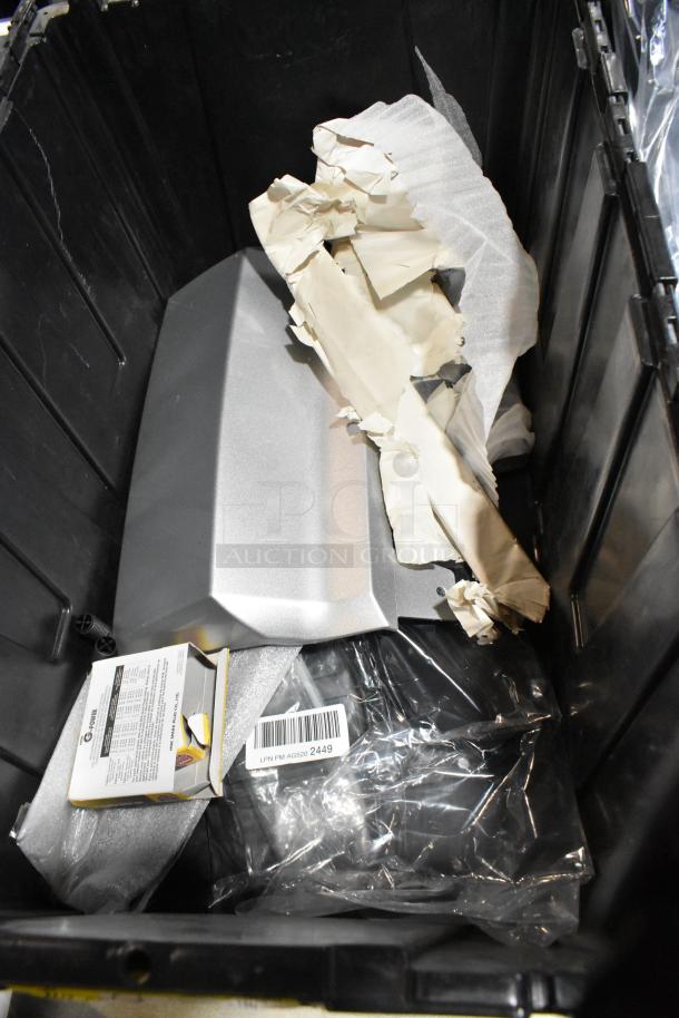 Black poly bin containing various items including a silver metallic object, crumpled paper, and a box with visible barcode "LPN PM AG520 2449."