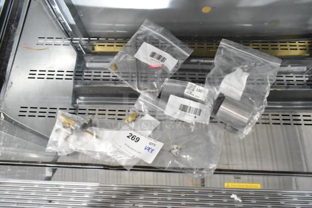 Five brand new kitchen appliance parts in bags, including Southbend hood fitting orifice, Moffat adjustable foot, Avantco thermal cutoff, American Range pilot tip, and burner gas valve. Each part tagged with product identification.