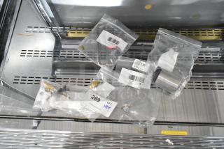 Five brand new kitchen appliance parts in bags, including Southbend hood fitting orifice, Moffat adjustable foot, Avantco thermal cutoff, American Range pilot tip, and burner gas valve. Each part tagged with product identification.