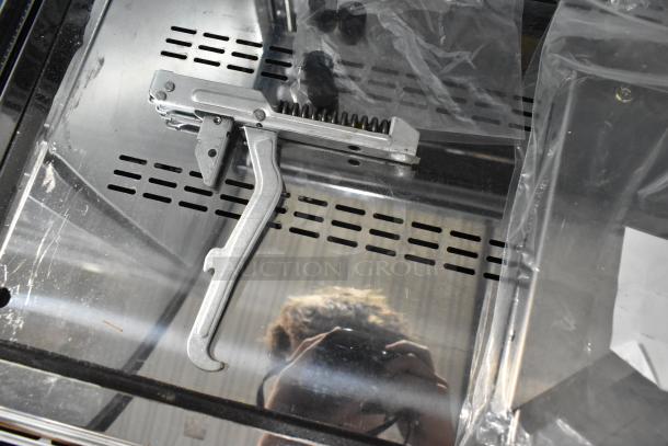 Metallic tool component with spring mechanism, reflective surface, and a clear plastic bag seen in an industrial setting.