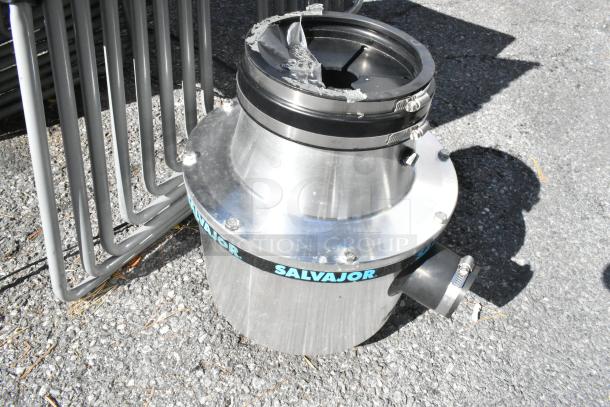 Salvajor 100 stainless steel commercial garbage disposal, 208/230/460 volts, exterior view on pavement, some wear visible.