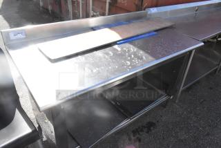 Stainless steel table with backsplash and under shelf, featuring signs of use. Visible tag indicates item number 301.