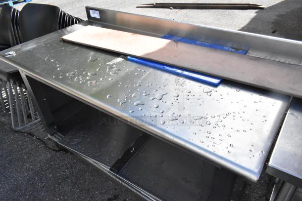 Stainless steel table with backsplash, featuring under shelf. Visible water droplets; used condition.