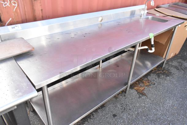 Stainless steel table with sink bay, back splash, and under shelf. Visible wear, includes faucet and drainage pipes. Lot tag 302.