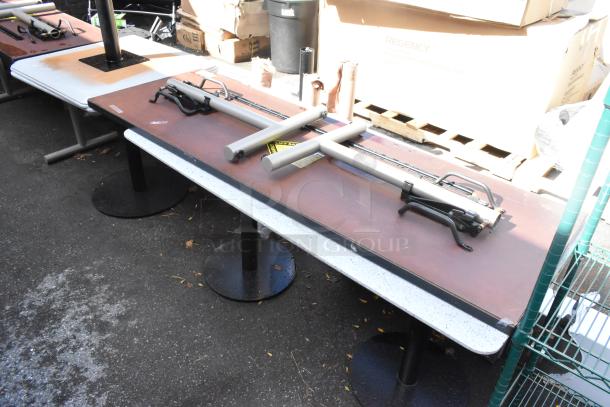 Two rectangular tables with laminate tops and black metal pedestal bases, in used condition. Disassembled parts placed on tables.