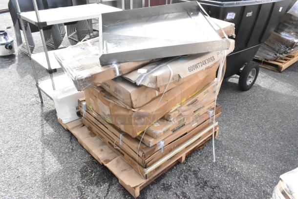 11 new scratch and dent commercial kitchen items stacked on a pallet, including Regency and Steelton stainless steel work tables.