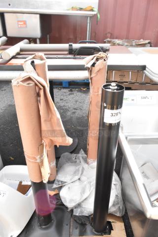 Four brand new black metal table base columns, partially wrapped, with minor scratches and dents visible.
