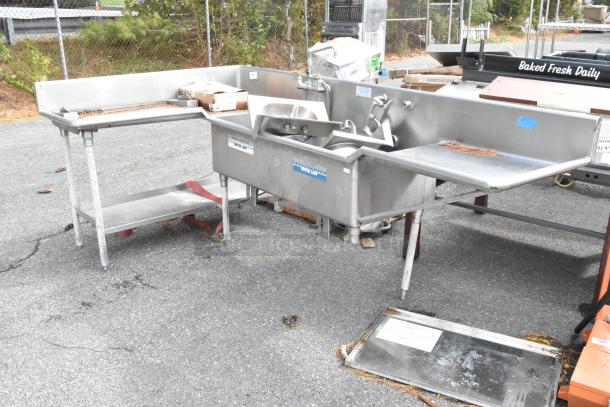 Stainless steel commercial L-shaped 3 bay sink with dual drain boards and under shelf, featuring visible faucets and labels.