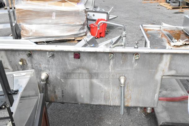 Stainless steel L-shaped 3 bay sink with dual drain boards and under shelf. Visible wear, taps and pipes attached. Ideal for commercial use.