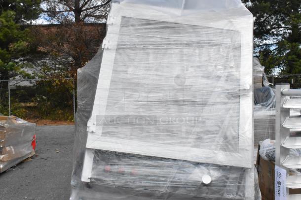 Plastic-wrapped pallet with assorted items, including frames and machinery, marked "BRAND NEW SCRATCH AND DENT." Outdoor setting.