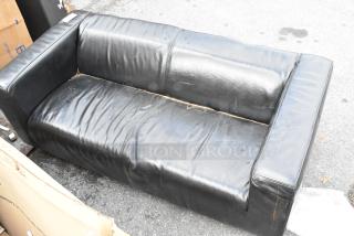 Black leather couch with armrests, visible wear and creases. No visible brand or markings, outdoor setting.