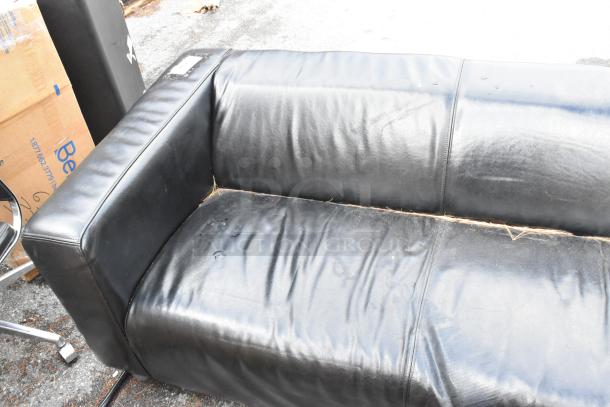 Black leather couch with armrests, visible wear and stains, outdoor setting, durable material, auction item.