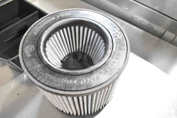 Air filter with visible pleats and a black rubber rim, inscribed with markings, on a metallic surface.