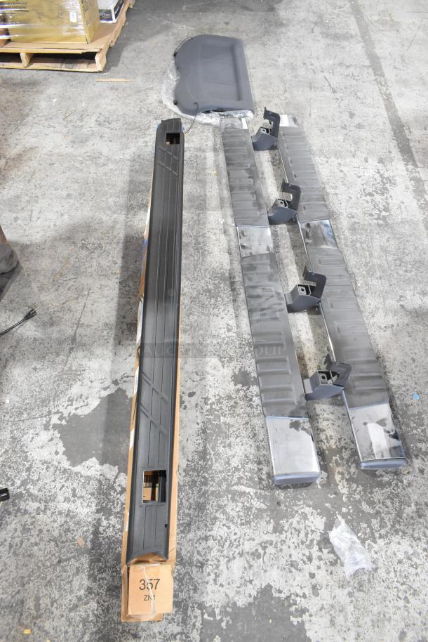 Four various car parts including a long black trim piece and multiple brackets, in good condition, positioned on a warehouse floor.