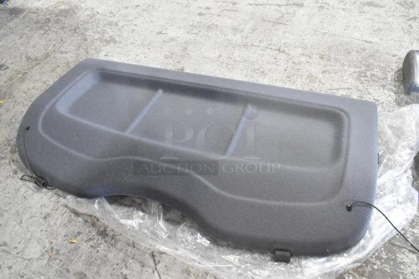 Gray car parcel shelf in excellent condition, textured surface, with attached cords, placed on protective plastic.