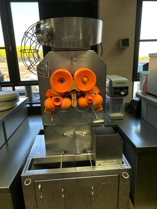 Citrocasa 8000 SB-ATS Advance Citrus Juicer in excellent condition; features stainless steel body and fruit holders; "AS IS" on label.