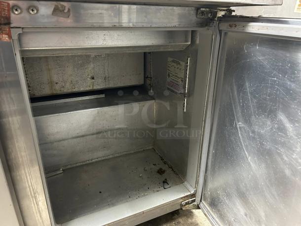 Interior view of Continental SW72-N-30M 3 Door Sandwich Prep Table showing storage space, label, and metal construction.