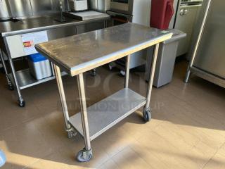 Stainless steel worktop table with casters, rounded edges, lower shelf. Great condition, commercial kitchen setting.