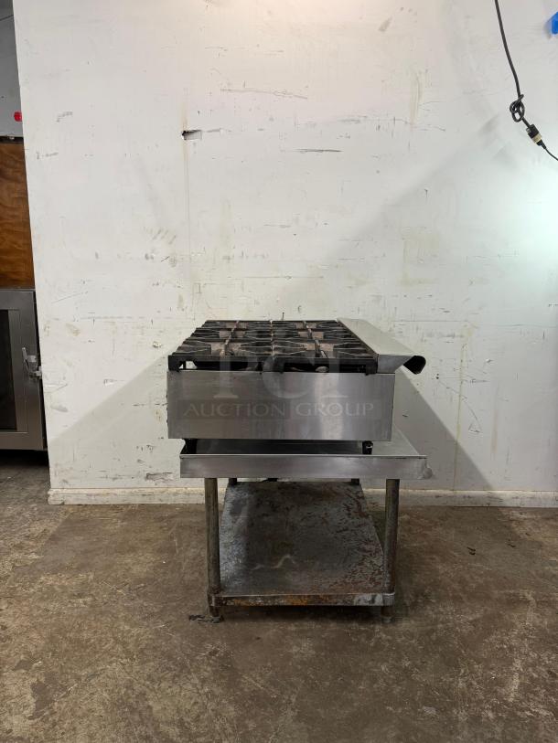 "Commercial 36-inch 6 burner range on metal stand, made of stainless steel, shows signs of use, industrial setting."