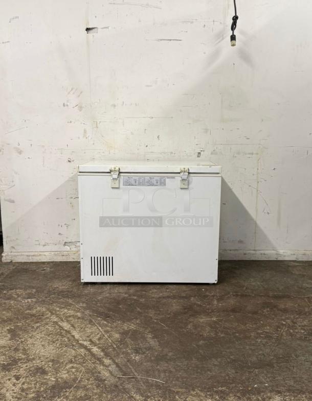 White deep freezer with metal latches, vent on the bottom left, and visible label. Worn, in fair condition.