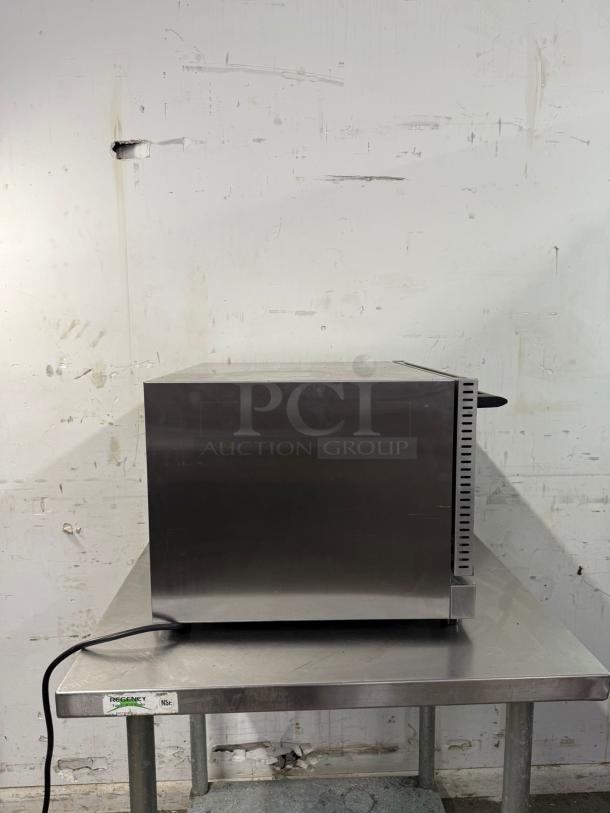 WINCO half-size countertop convection oven, stainless steel, side view, on a metal table, 120v power cord visible.