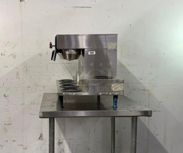 Brand new BUNN Axiom 0/6 Twin Coffee Brewer with 6 lower warmers, stainless steel body on a metal table.