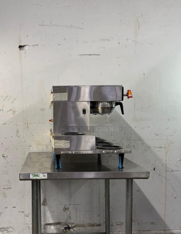 BRAND NEW Bunn Axiom 0/6 Twin 12 Cup Automatic Coffee Brewer with six lower warmers on a metal table.