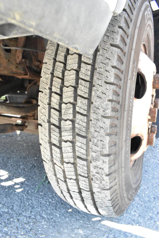 Close-up of a tire on a 2004 Isuzu Morgan Diesel Reefer Box Truck with visible tread pattern and some rust on the wheel.
