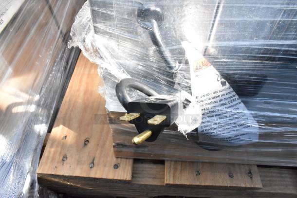 Plastic-wrapped electrical cord plug on wooden pallet; warning label partially visible, indicating safety instructions.