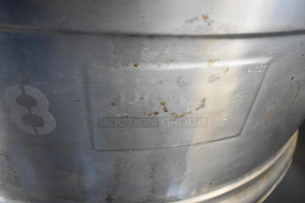 Stainless steel commercial kettle with agitator, floor style, visible markings, some wear and discoloration.
