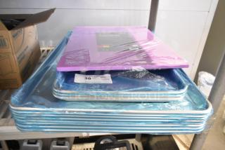 Stack of scratch and dent kitchen items including Choice purple cutting board and aluminum sheet pans, still in packaging.