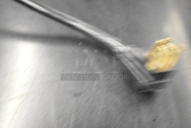 Blurry image depicting an electrical cord plug on a stainless steel surface. Item details not visible.