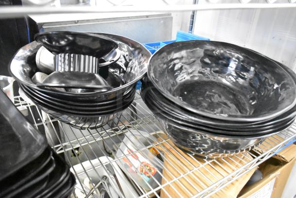 Black plates and bowls stacked on a wire shelf, including a poly bin. Items appear in good condition. Shelving unit not included.