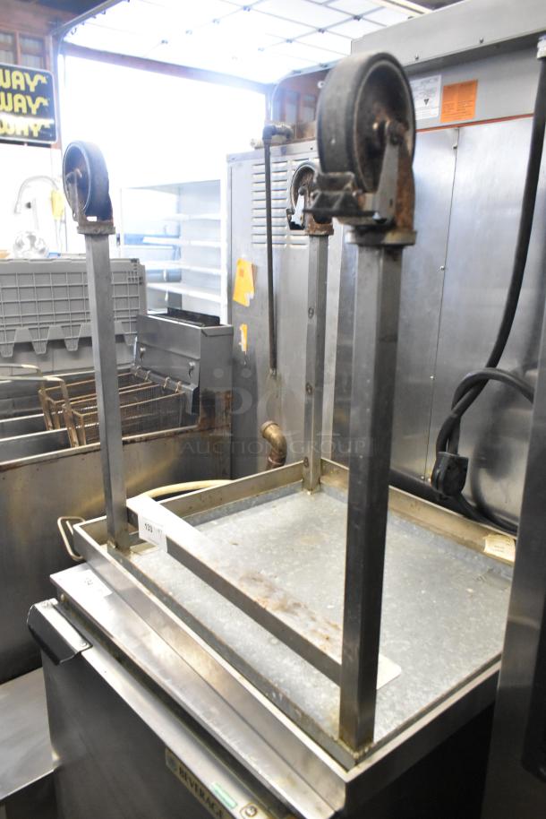 Stainless steel equipment stand on commercial casters, rust visible, sturdy metal construction, ideal for industrial use.