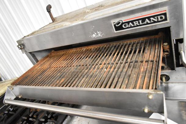 Garland stainless steel commercial cheese melter with gas operation, featuring table, backsplash, and undershelf. Visible wear.