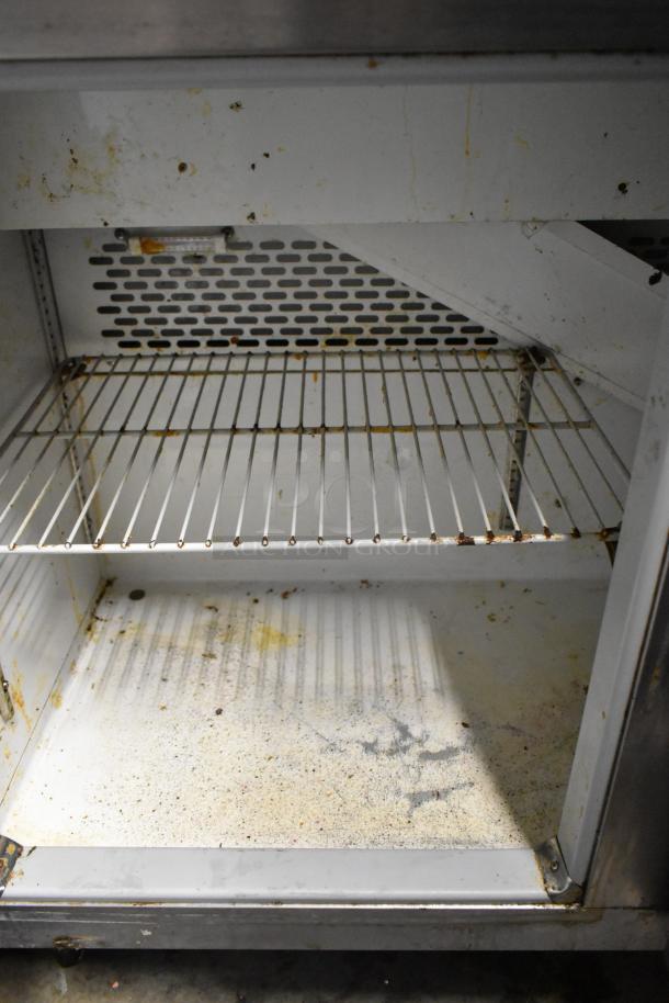 Migali CA412 stainless steel commercial prep table interior, showing wire shelf and some visible wear and residue.