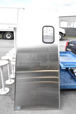 Stainless steel swinging kitchen door with window, used condition, minor scratches visible. Ideal for commercial use.