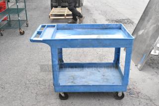 Blue two-tier poly cart on commercial casters, used condition, features handle and sturdy shelves, ideal for transport.