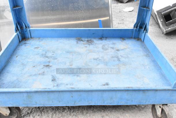 Blue poly 2-tier cart with commercial casters showing signs of wear. Ideal for industrial use.