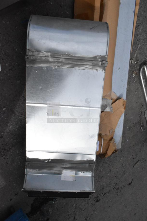 Metal duct, silver, slightly bent edges, small label with specs attached. Appears to show signs of use.