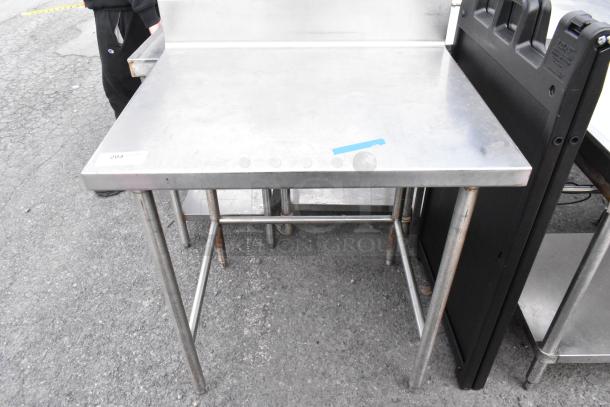 Stainless steel table with backsplash, good condition, four legs, slight wear marks, inventory tag visible.