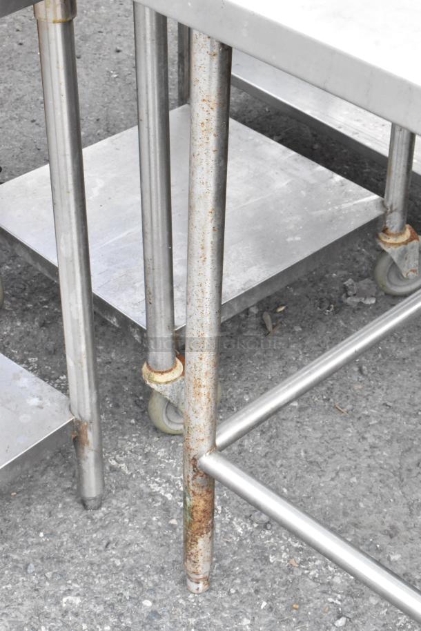 Stainless steel table with back splash, features caster wheels and some surface rust, ideal for commercial kitchen use.