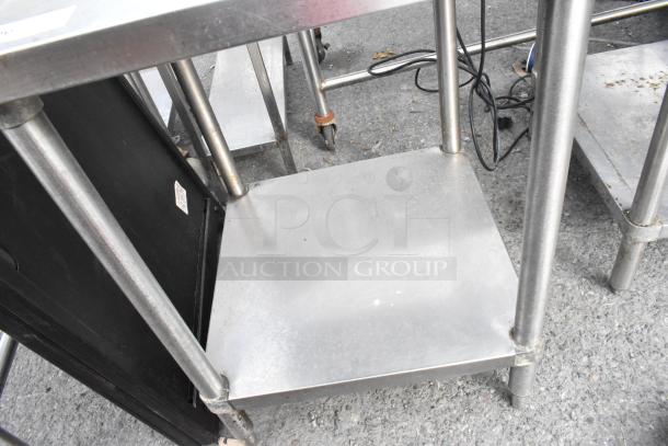 Stainless steel table with under shelf, sturdy design, slightly worn surface, cylindrical legs, suitable for kitchen or workshop.