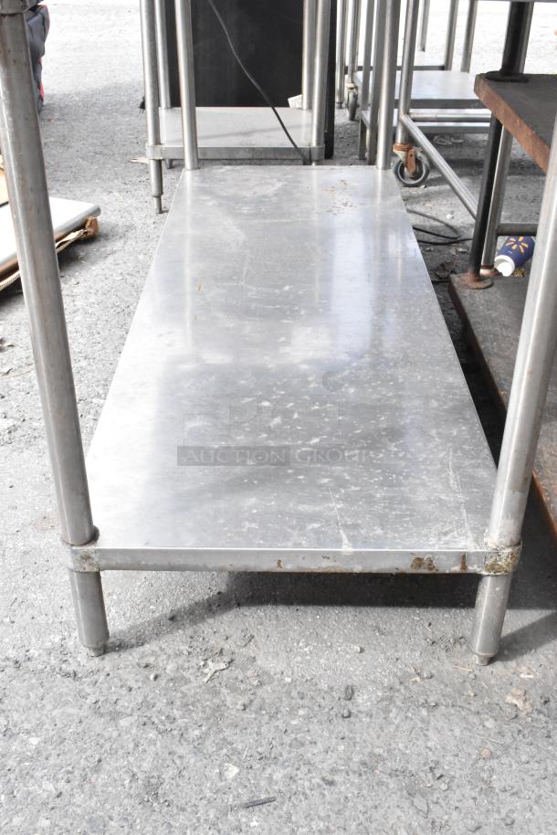 Stainless steel table with back splash and under shelf, showing signs of use, suitable for commercial kitchens.