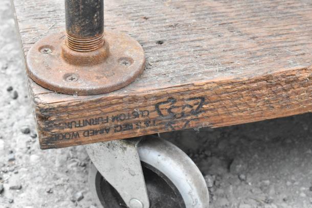 Wood and metal 3-tier cart on commercial casters, rustic finish, visible industrial markings on wood, sturdy construction.
